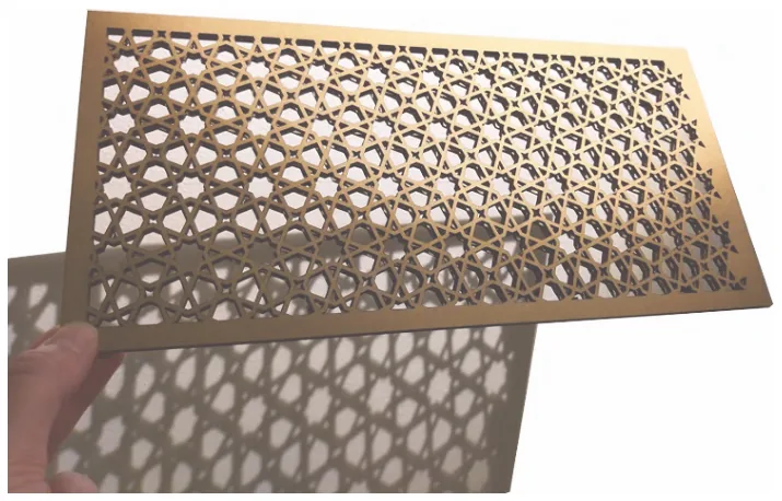 A hand holding a milled Tricoya shutter panel with an intricate perforated pattern, casting a patterned shadow